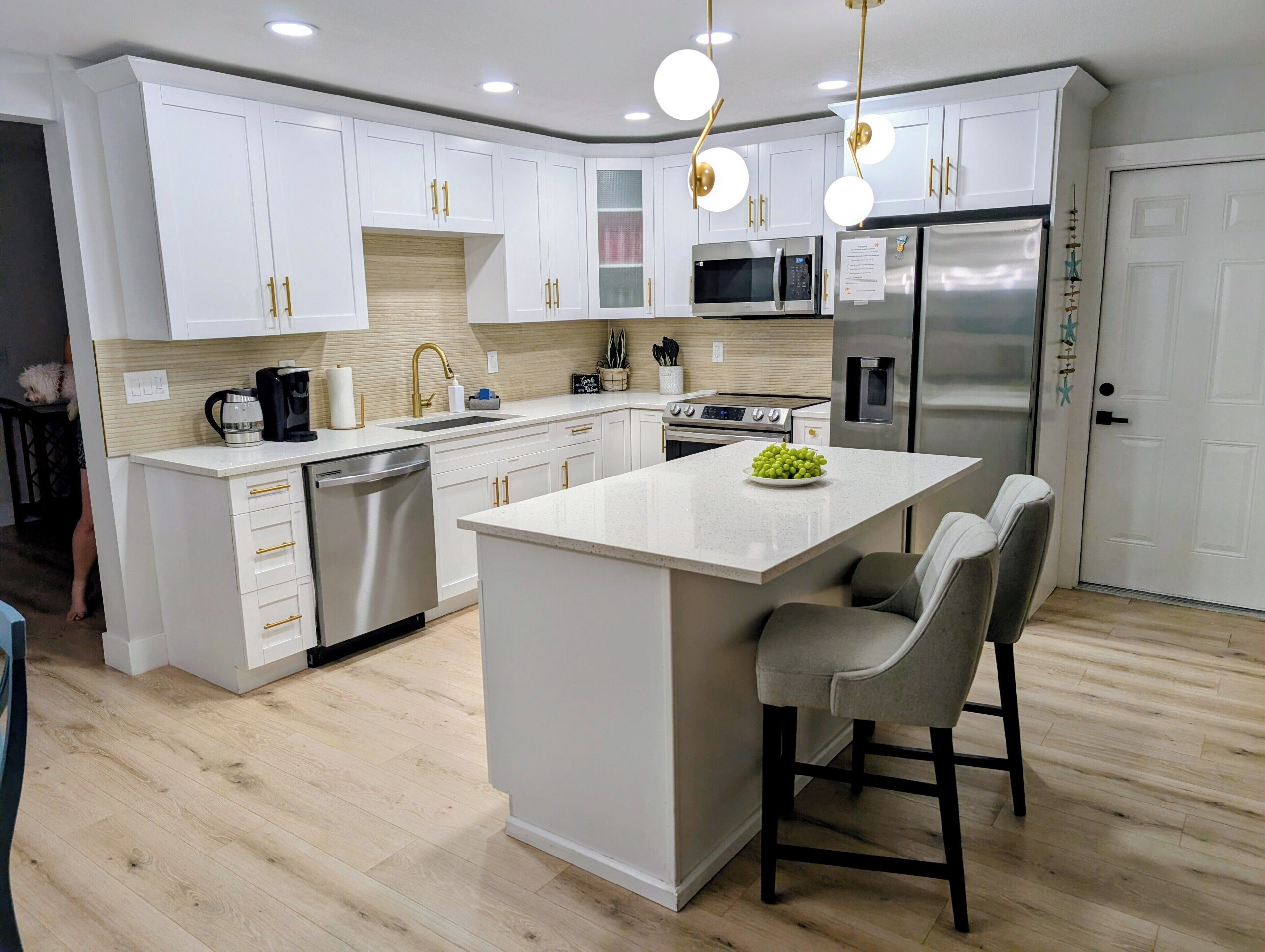 A modern kitchen with white cabinetry, stainless steel appliances, and a central island with bar stools.