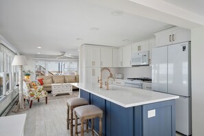 A modern kitchen with white cabinets, a stainless steel refrigerator, and a central island with stools. - WATCH THE SUNSET FROM YOUR Beautiful 5-bedroom home with AC Beach Haven Crest (Beach Haven)
