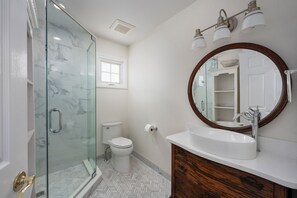 A bathroom with a glass shower enclosure, a toilet, a sink with a wooden vanity, and a mirror with a wooden frame. - WATCH THE SUNSET FROM YOUR Beautiful 5-bedroom home with AC Beach Haven Crest (Beach Haven)