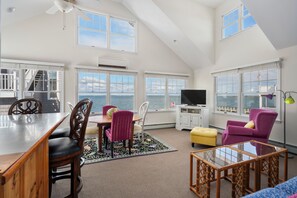 A spacious living area with a large dining table, multiple chairs, a television, and a view of the sea through large windows. - WATCH THE SUNSET FROM YOUR Beautiful 5-bedroom home with AC Beach Haven Crest (Beach Haven)