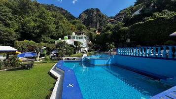 Piscina con cubierta azul, rodeada de vegetación exuberante y montañas.