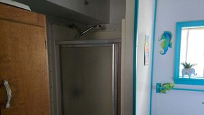 A bathroom with a shower, a wooden cabinet, and a window with a plant. - Peaceful 1-bedroom house with AC in charming Pittsburg within walking of PSU (Pittsburg)