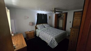 A bedroom with a bed, a nightstand, a lamp, a wardrobe, and a ceiling fan.