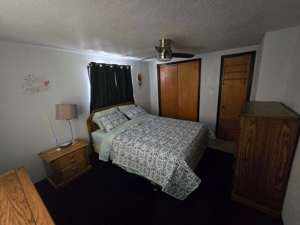 A bedroom with a bed, a nightstand, a lamp, a wardrobe, and a ceiling fan.