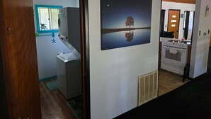 A hallway with a bathroom, a wall-mounted heater, and a door leading to another room.