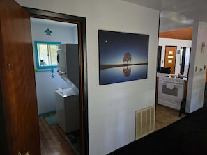 A hallway with a bathroom, a wall-mounted heater, and a door leading to another room.