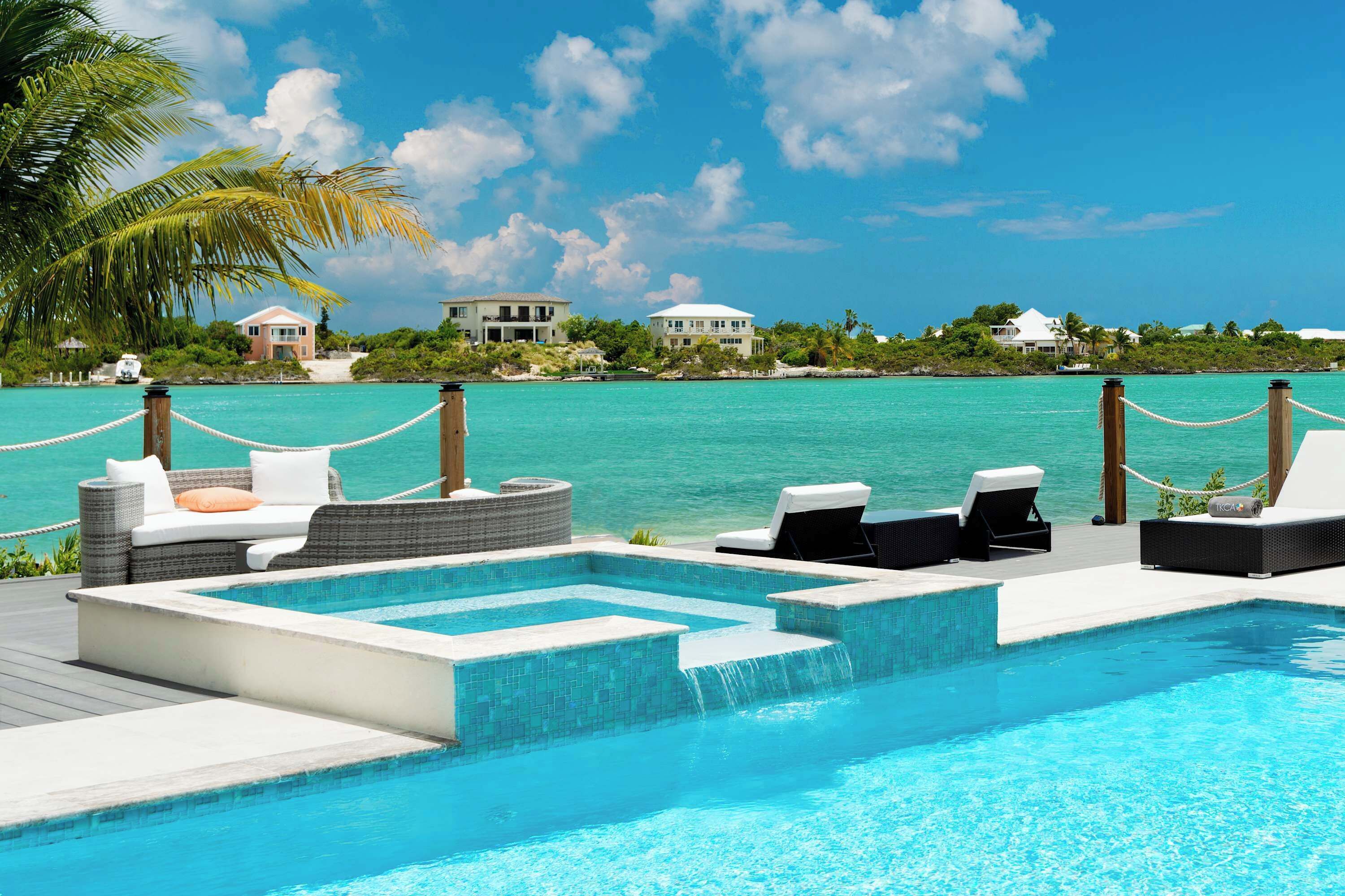 A pool area with lounge chairs and a hot tub, surrounded by a wooden deck and a view of the ocean.