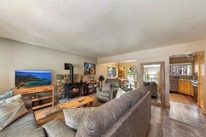 Ein gemütliches Wohnzimmer mit Kamin, einer Couch, einem Couchtisch und einem Fernseher, der eine schöne Aussicht zeigt.