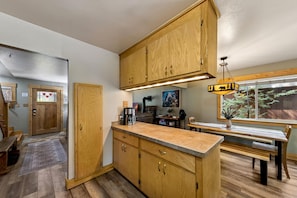 A kitchen with wooden cabinets, a coffee maker, and a dining area with a bench. - BTLR- Tahoe Pines Retreat | 4BR 2BA Cabin (South Lake Tahoe)