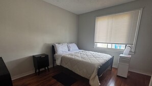 Un dormitorio con cama, mesita de noche, calefactor y ventana con persianas.