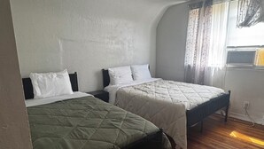 Una habitación con dos camas, ventilador de techo y ventana con cortinas.