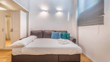 Un dormitorio con cama, almohadas y una ventana con persianas.