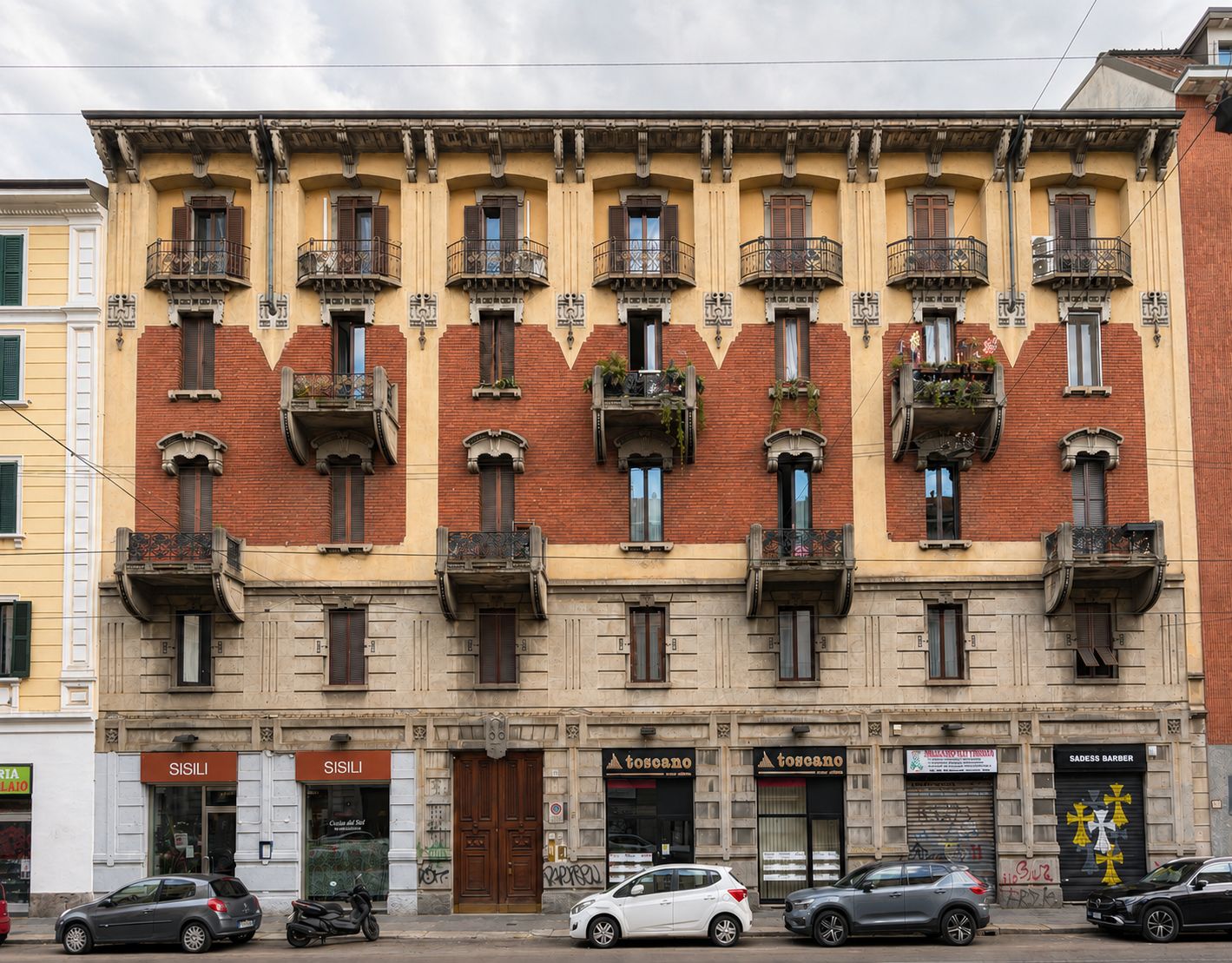 Un edificio de varios pisos con balcones, comercios en la planta baja y automóviles estacionados al frente.