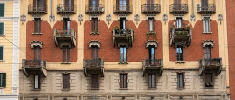 Un edificio de varios pisos con balcones, comercios en la planta baja y automóviles estacionados al frente.