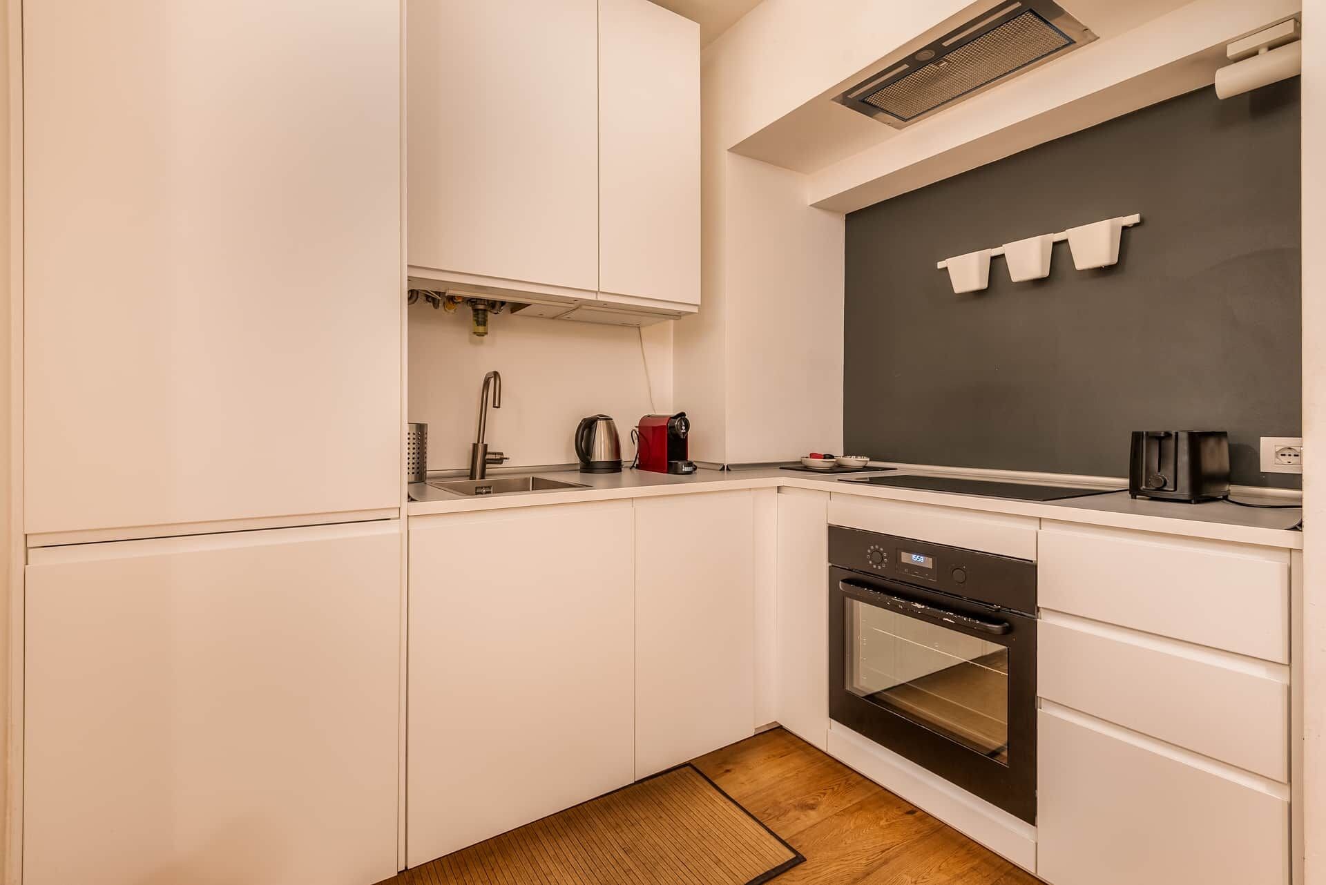 Una cucina moderna con mobili bianchi, forno integrato e zoccolo nero.