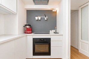 Una cocina compacta con horno integrado, tope de inducción rojo y salpicadero gris.