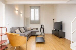 Una sala de estar moderna con un sofá modular, una mesa de centro de vidrio, un televisor sobre un mueble bajo y una estantería metálica roja.