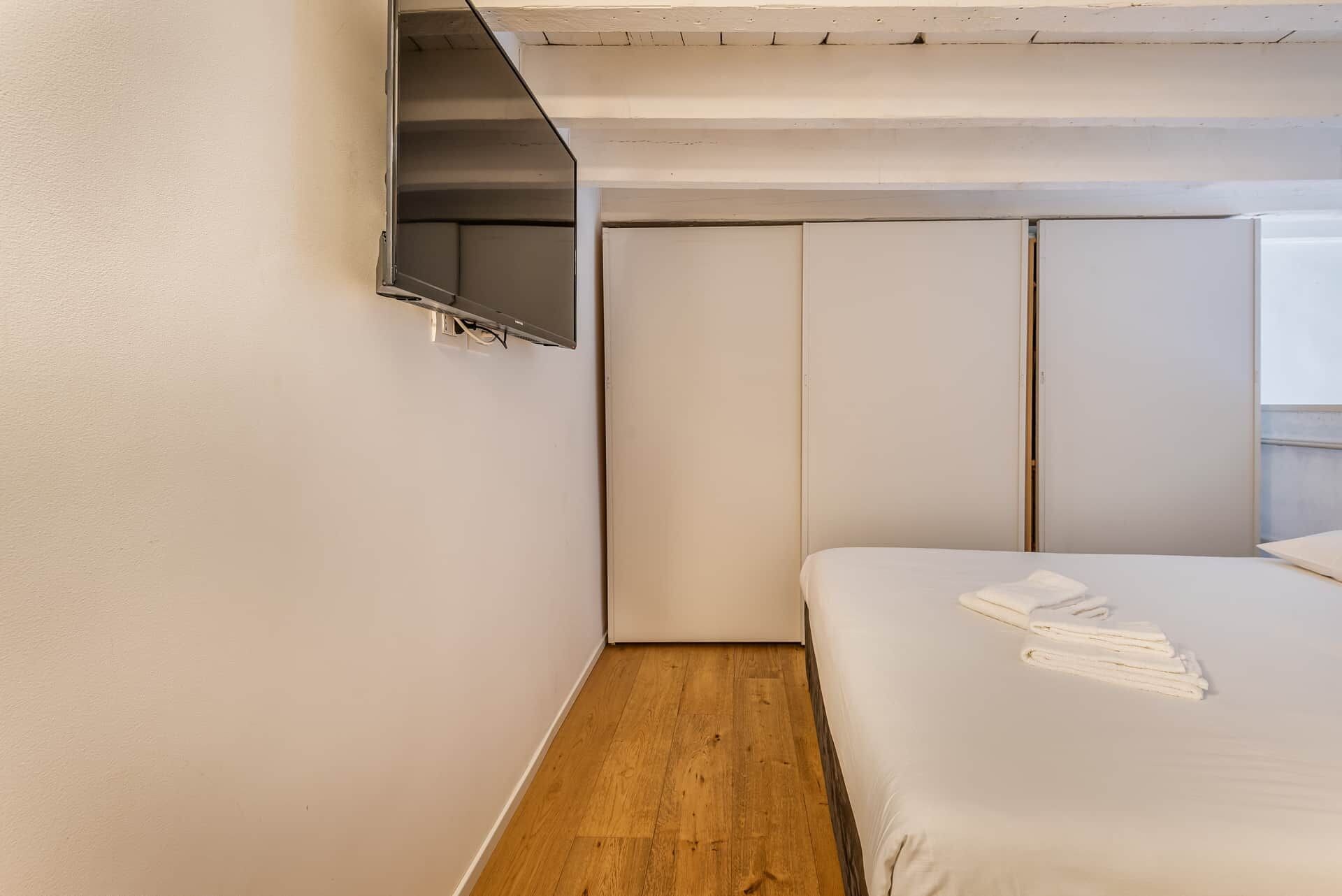 A bedroom with a bed, a TV mounted on the wall, and a wooden floor.