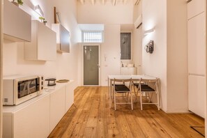 A compact kitchen with a dining area, wooden flooring, and a view of the living space through an open door. - Cozy Apartment Milano | Bocconi & City Center (Milan)