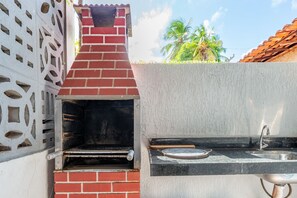 A brick-built outdoor oven with a metal grate, a metal sink, and a wooden cutting board. - Casa Maragogi- 2Qrts e Piscina-SH162 (Maragogi)
