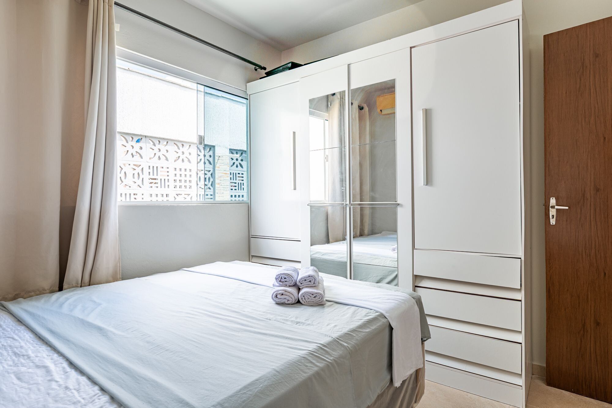 A bedroom with a bed, a wardrobe, and a window with a view of a building.