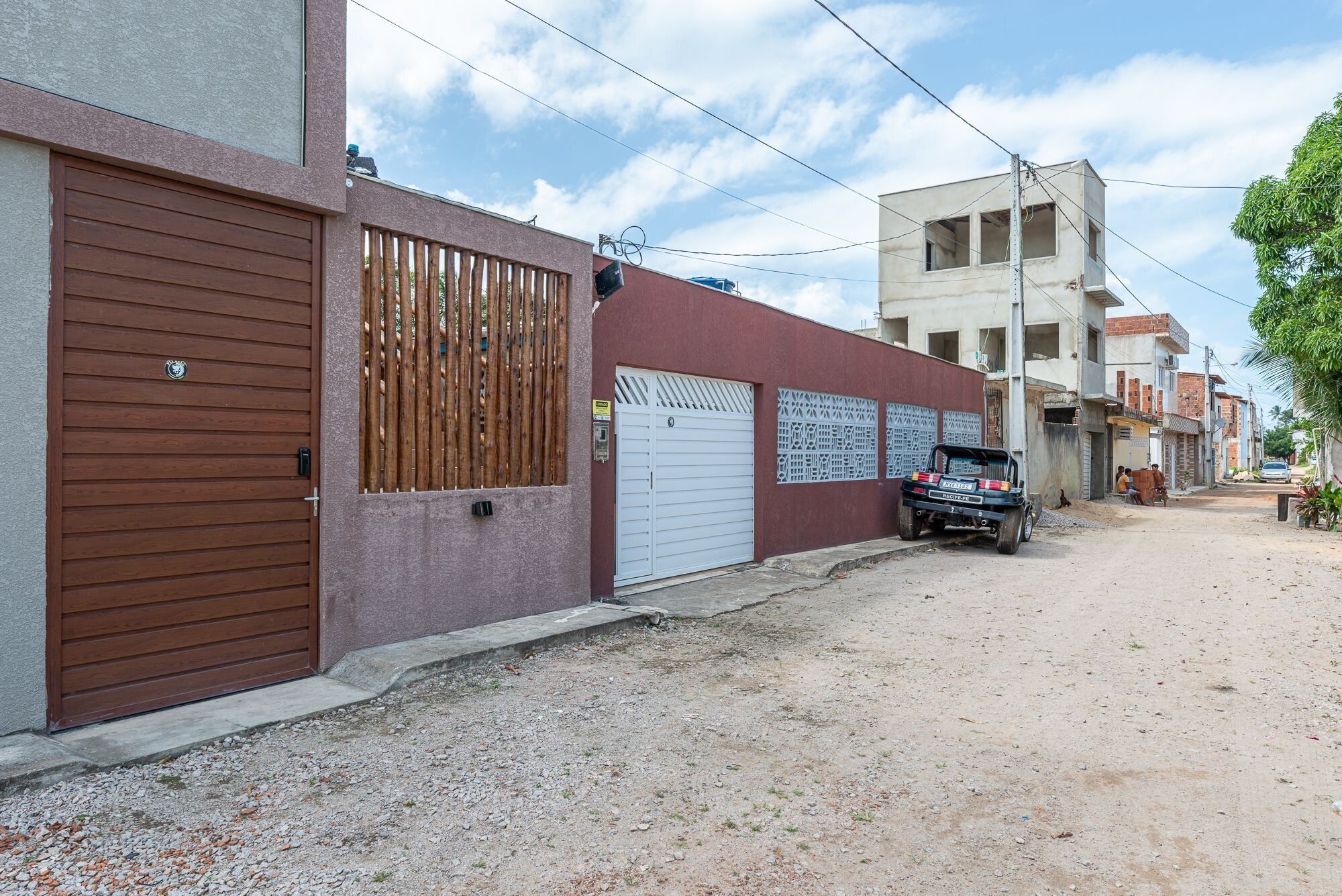 Rua residencial com casas, uma caminhonete estacionada e uma estrada de terra.