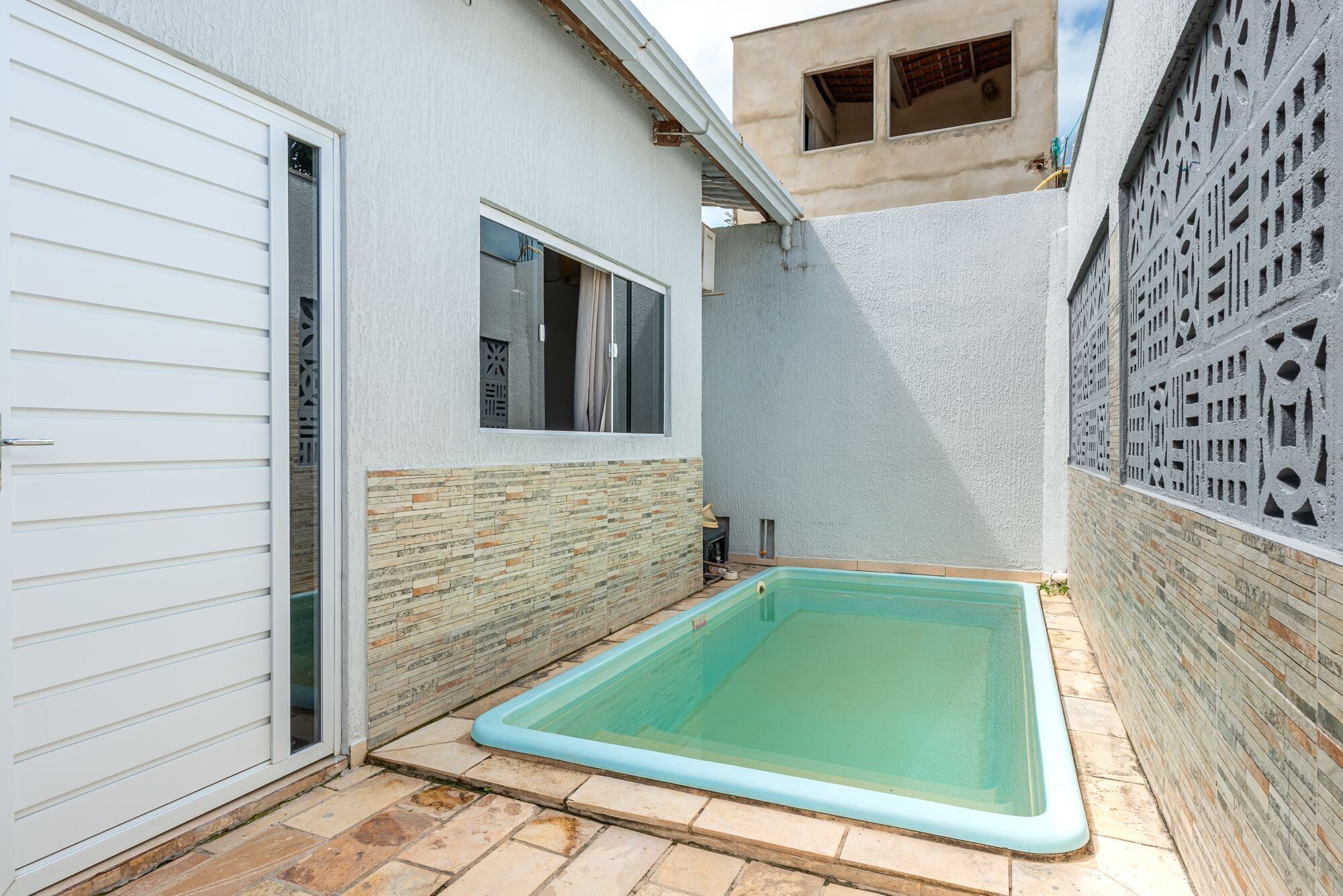 Una piscina con un borde de baldosas, una puerta de garaje blanca y una ventana con vista a un edificio.