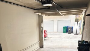 Een garage met een betonnen vloer, een rode auto op afstand en een witte deur.