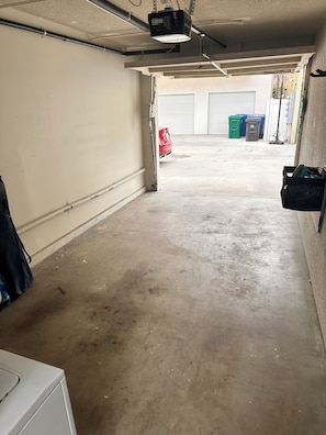 A garage with a concrete floor, a red car parked in the distance, and a white door. - 2BDR Belmont Shore Retreat <> Steps from the Beach (Long Beach)