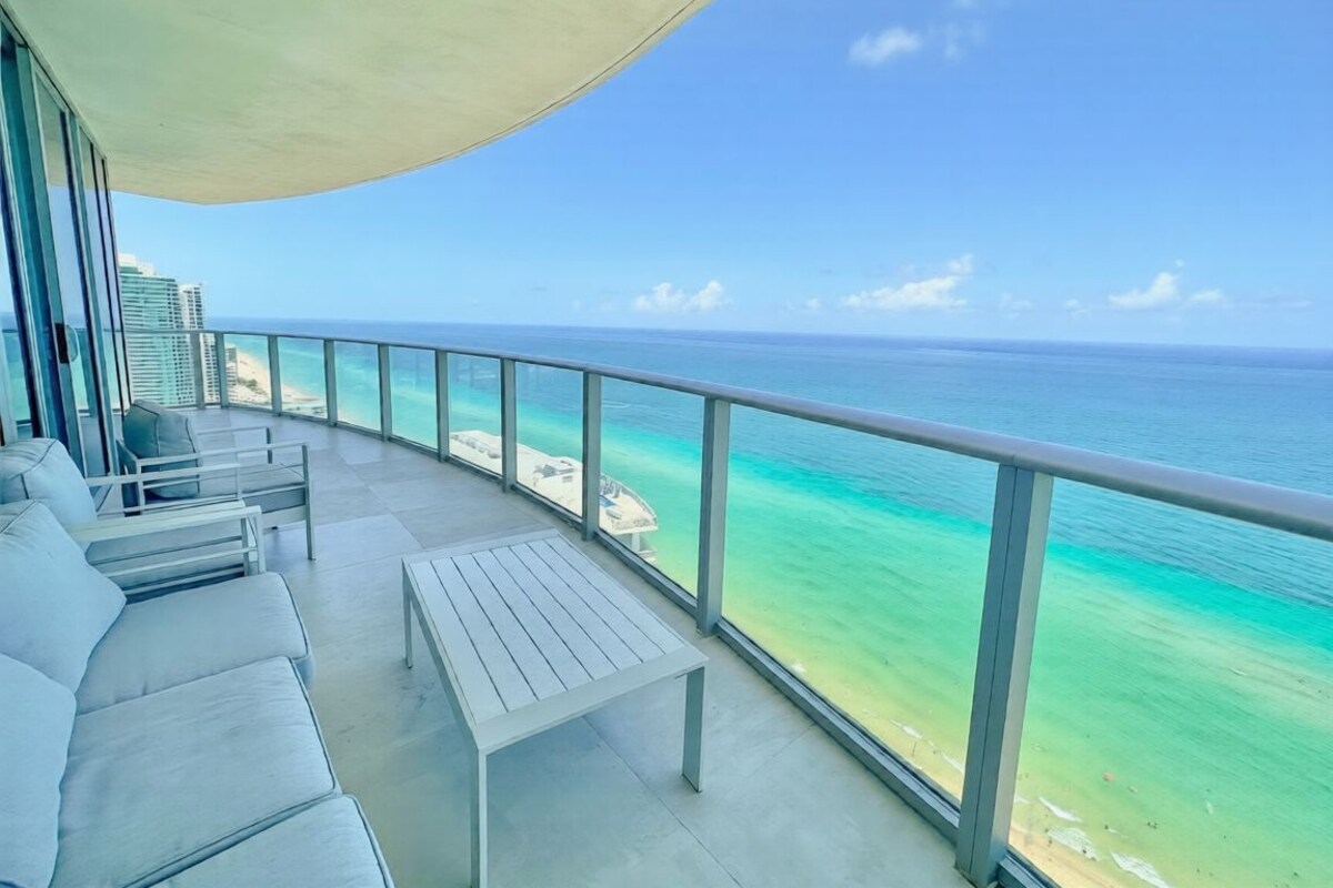 A balcony with a view of the ocean, a white sofa, and a small table.