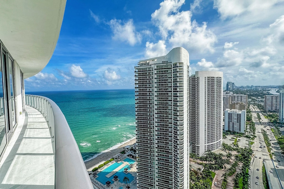 A high-rise building with a curved facade overlooking a beach and ocean.