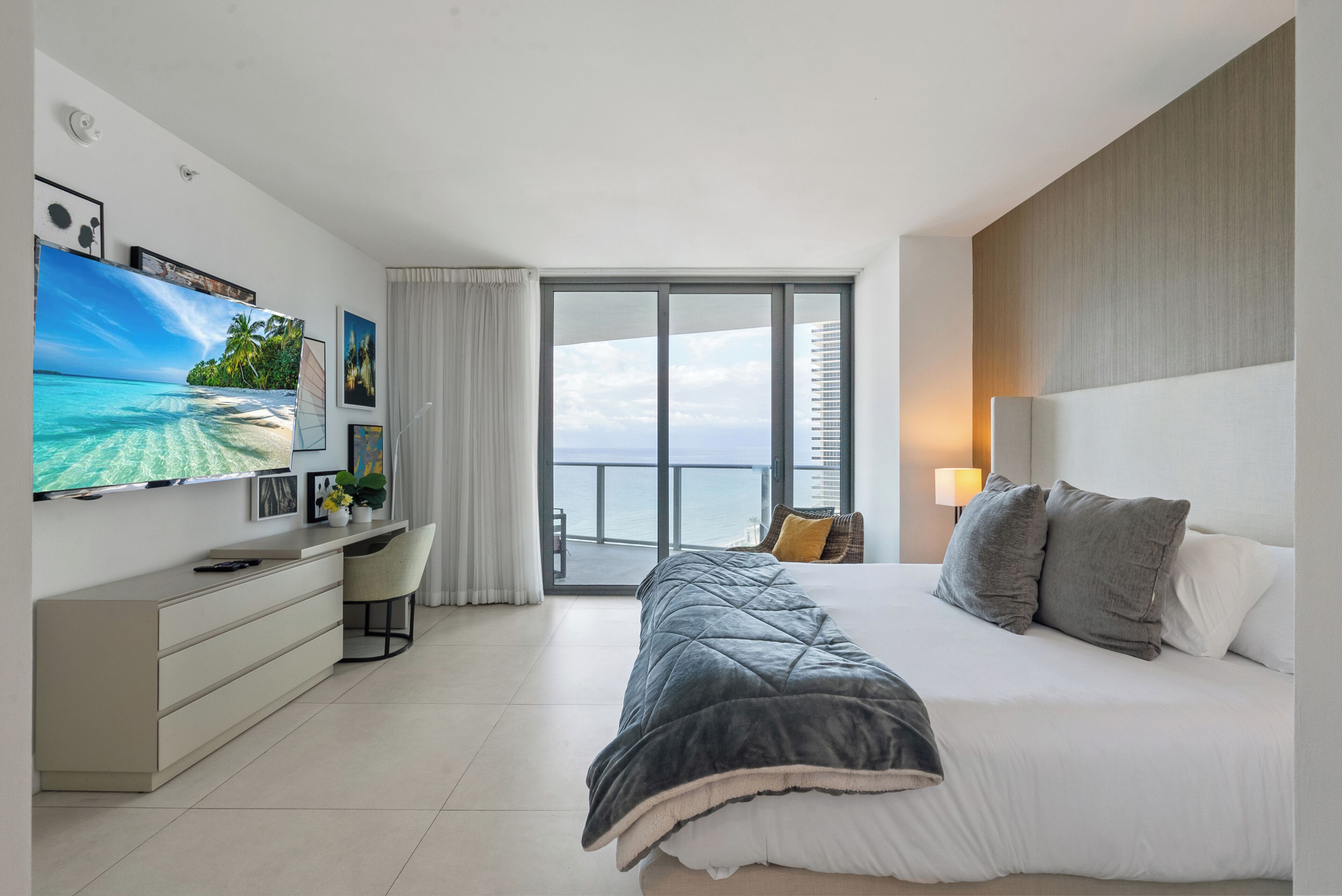 Une chambre d’hôtel moderne équipée d’un lit, d’un bureau, d’une télévision et d’un balcon avec vue sur la mer.