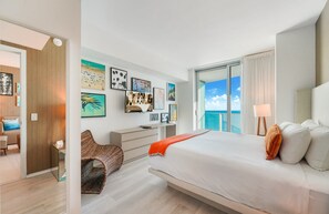 A modern hotel room with a large bed, a desk, and a view of the ocean.