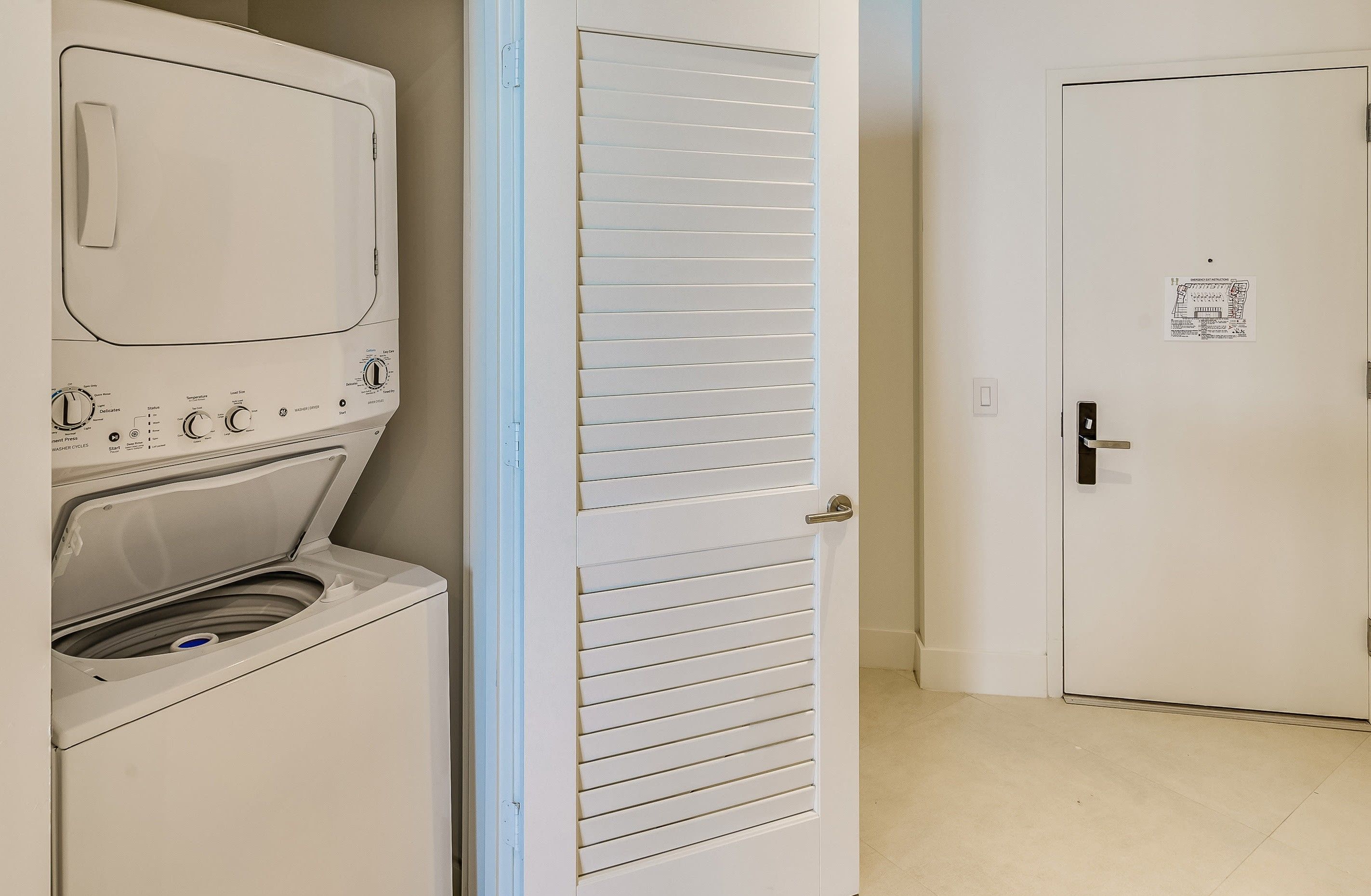 A laundry room with a washing machine and dryer, a door with a window, and a tiled floor.