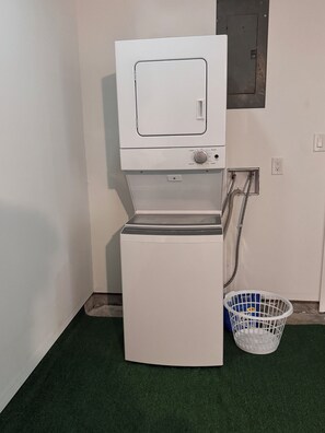 Une machine à laver compacte, blanche, conçue pour être fixée au mur, dotée d’un panneau de commande et d’un tuyau d’arrivée d’eau.