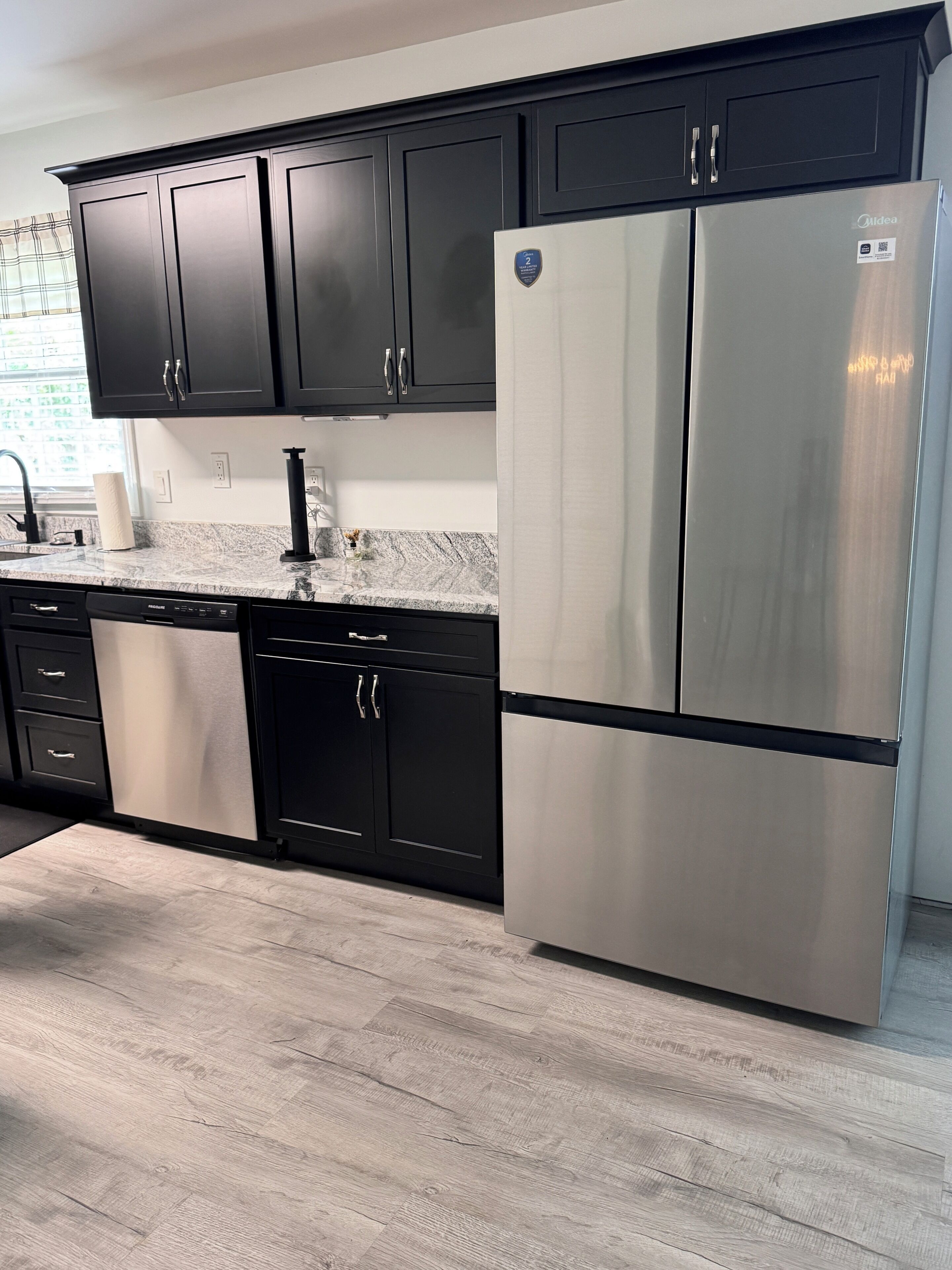 Una cocina con gabinetes negros, electrodomésticos de acero inoxidable y encimera de mármol.