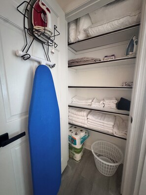 A laundry area with an ironing board, shelves with folded towels, and a basket. - Welcome to your modern, cozy, family-friendly home away from home in Savannah,Ga (Savannah)