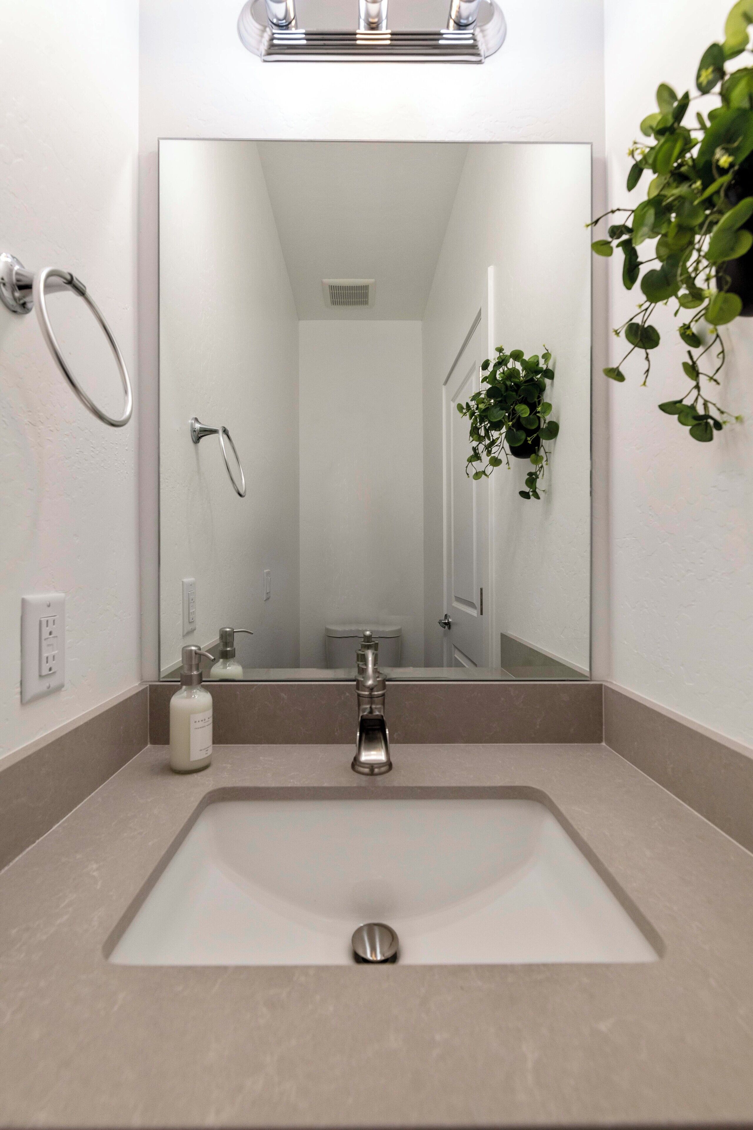 A bathroom with a large mirror, a sink, a towel ring, a potted plant, and a toilet.
