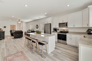 A modern kitchen with white cabinets, stainless steel appliances, and a central island with bar stools. - Where Comfort Meets Nature! Cozy Modern 2BR Suites with Garage & Patio  (Payson)