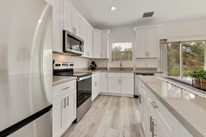 A modern kitchen with white cabinetry, stainless steel appliances, and a large window providing natural light. - NEW LISTING SALE: Peaceful 2BD/2.5BA Townhome w/ Forest Setting, Patio, & Garage (Payson)