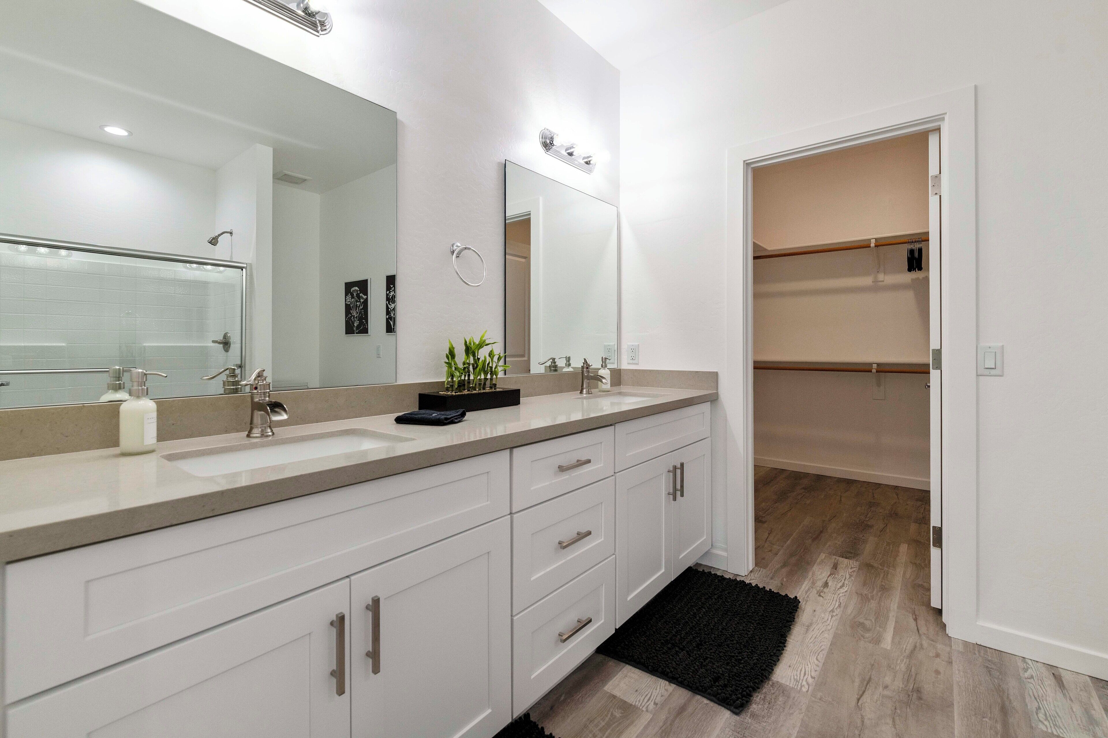 Ein modernes Badezimmer mit einem großen Spiegel, zwei Waschbecken, einer Dusche und einem begehbaren Kleiderschrank.