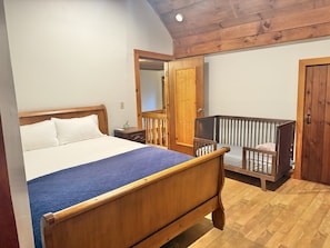 A bedroom with a wooden bed, a nightstand, a crib, and a wooden door.