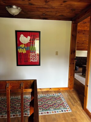 Ein Zimmer mit Holzboden, einem gerahmten Poster an der Wand, einer hölzernen Bank und einem gemusterten Teppich.