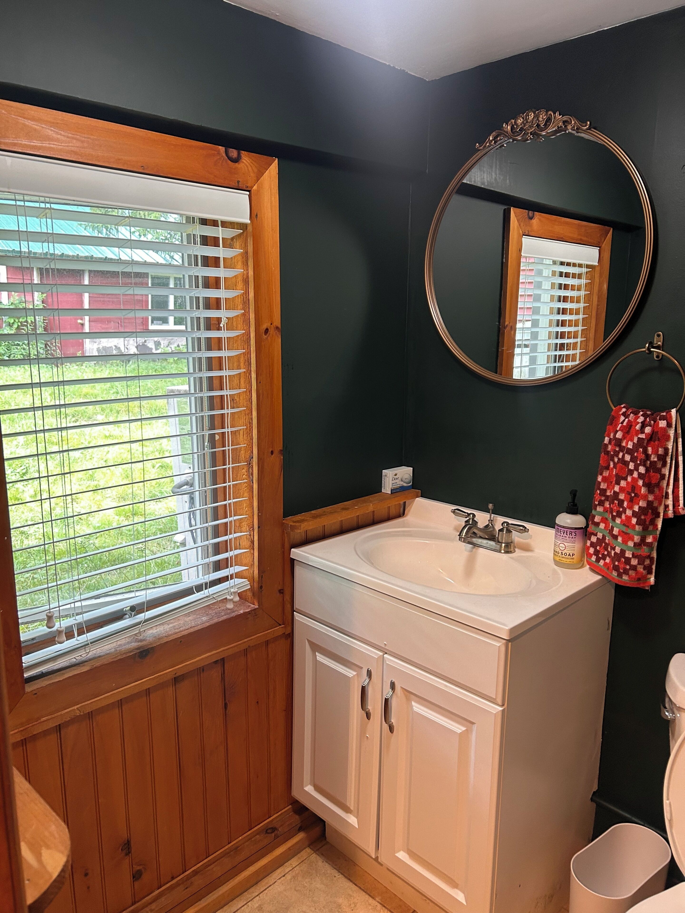 A bathroom with a wooden vanity, a sink, a mirror, and a window with blinds.