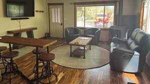 A living room with a wooden table, bar stools, a sofa, and a fireplace. - Large Backyard, River Views & Mountain Adventures (Gunnison)