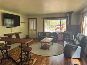 A living room with a wooden table, bar stools, a sofa, and a fireplace. - Large Backyard, River Views & Mountain Adventures (Gunnison)