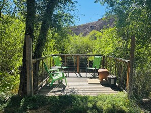 A wooden deck with green chairs and a table, surrounded by a wire fence and lush greenery. - Large Backyard, River Views & Mountain Adventures (Gunnison)