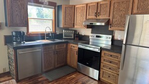 A kitchen with wooden cabinets, stainless steel appliances, a window, and a ceiling fan. - Large Backyard, River Views & Mountain Adventures (Gunnison)
