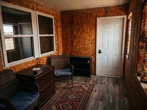 A room with a wooden wall, a white door, a patterned rug, a wicker sofa, and a small table.