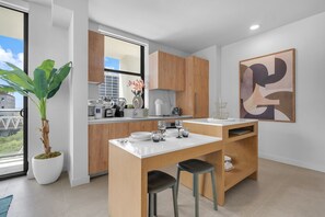 A modern kitchen with a central island, wooden cabinets, and a large window. - The Crosby Miami Worldcenter (Miami)